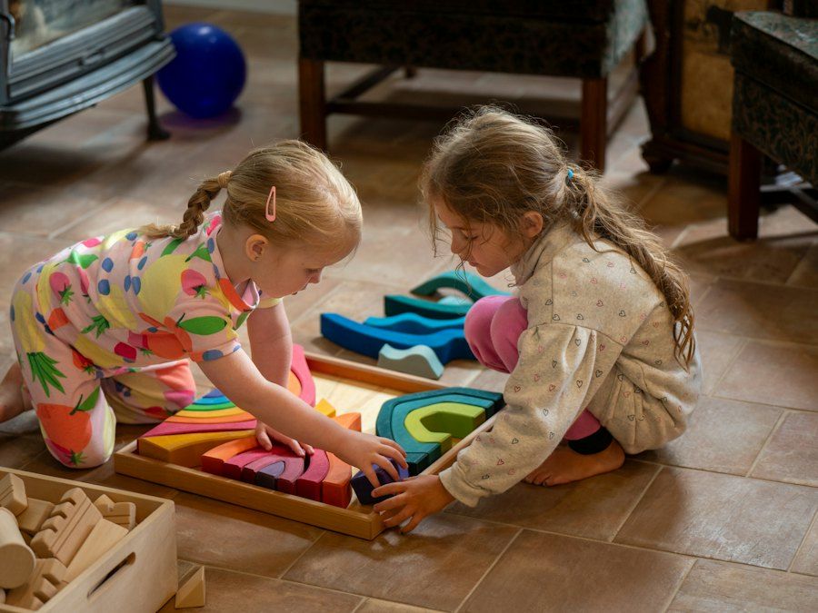 Zwei Mädchen spielen auf dem Boden mit bunten Holzblöcken